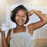 Milk, portrait and African girl with muscle from healthy drink for energy, growth and nutrition in the kitchen. Happy, smile and child flexing muscles from calcium in a glass and care for health